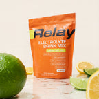 variant:49281673330925 Orange Relay Electrolyte Drink Mix package with lemons and limes on a light background